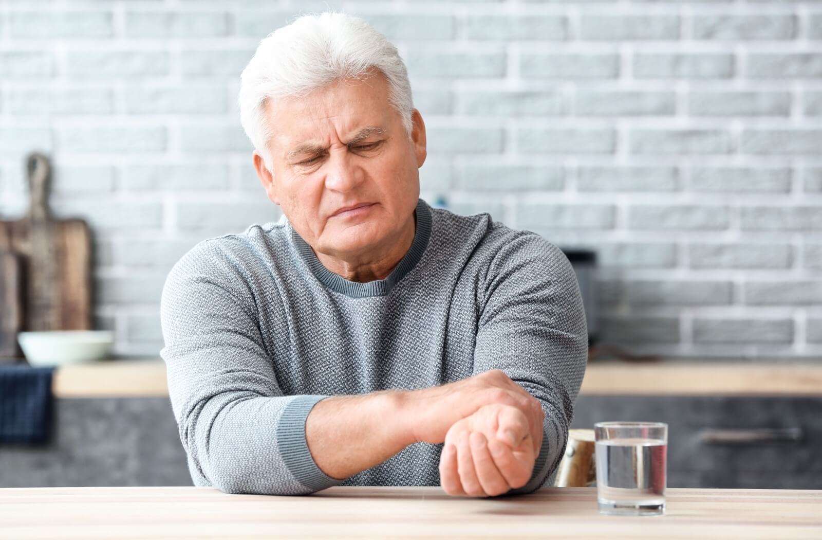 An older adult man holding his wrist to control his tremors.