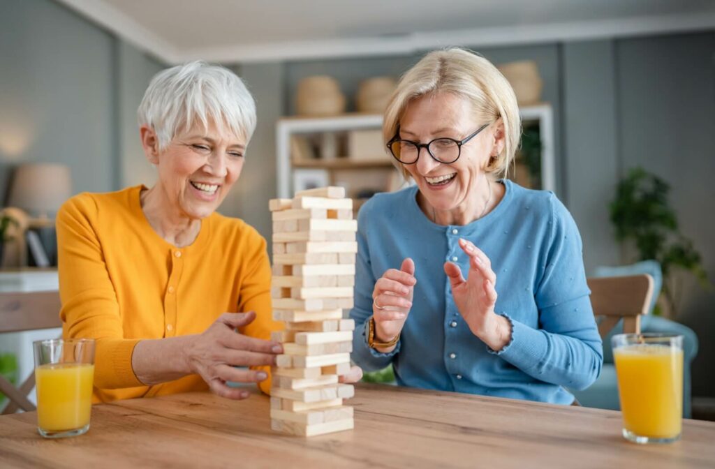 Two smiling older adults play a game of Jenga together.
