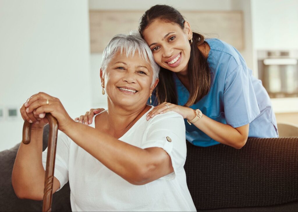 a caregiver holding a senior with a cane sitting on a sofa in personal care
