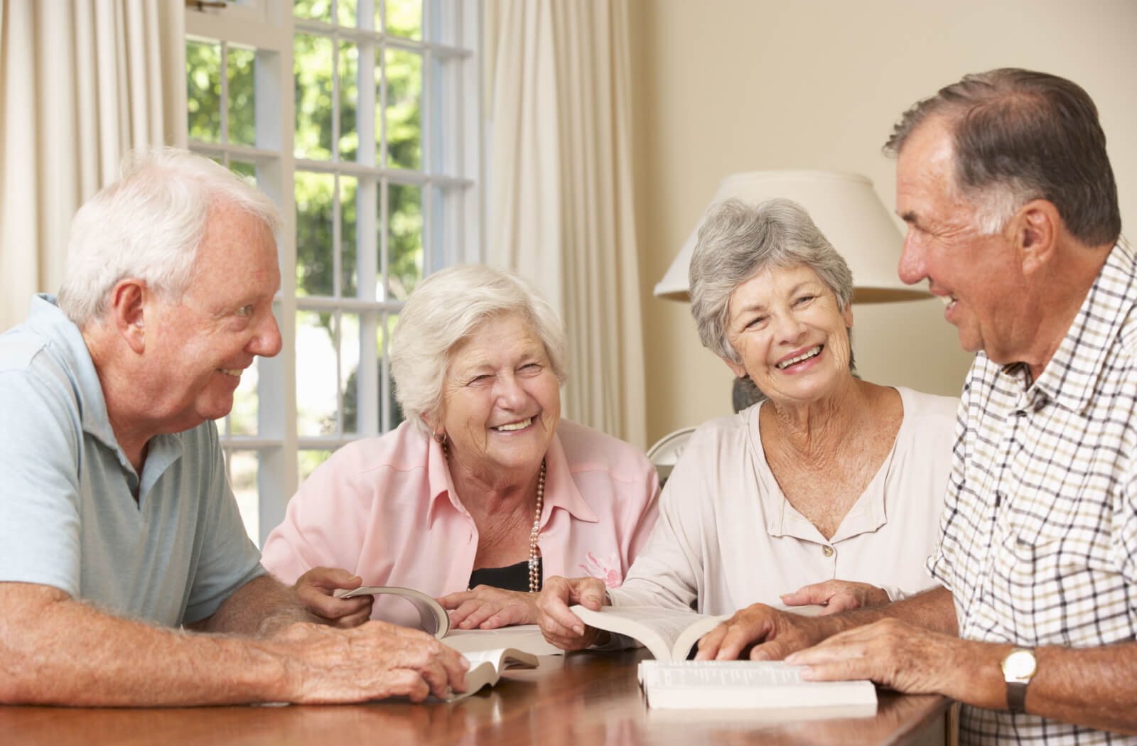 Four older adults laughing around a table with open books during their book club session.